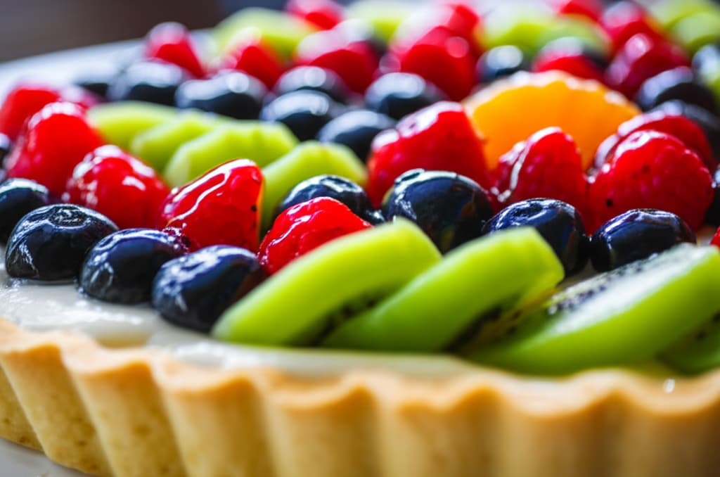 A vibrant, freshly baked fruit tart with an assortment of colorful berries, kiwi, and citrus slices on a creamy filling, showcased on a golden crust. Perfect for a delicious homemade dessert.